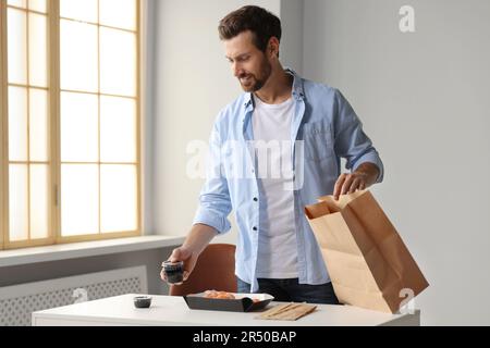 Homme qui a déballé sa commande du restaurant sushi à la table dans la salle Banque D'Images