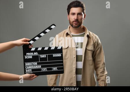 L'acteur se produit alors que la deuxième caméra de l'assistant tient le clapperboard sur fond gris Banque D'Images