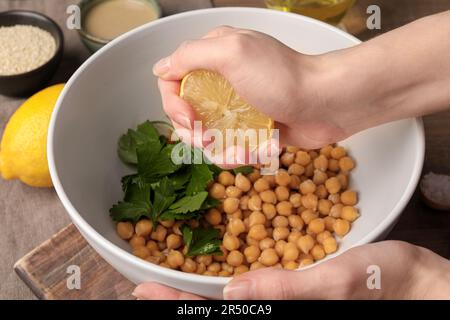 Femme pressant le jus de citron sur les pois chiches à la table, gros plan. Cuisson de délicieux houmous Banque D'Images