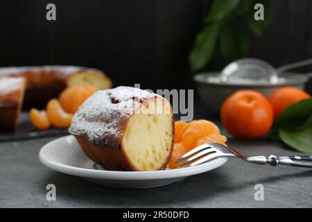 Morceau de délicieux gâteau au yaourt maison avec sucre en poudre et mandarines sur table grise Banque D'Images