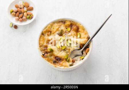 Dessert arabe traditionnel Umm Ali sous forme de céramique blanche décorée de noix sur fond gris clair, vue du dessus Banque D'Images