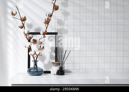 Diffuseur en roseau, bougie et branches en coton avec fleurs moelleuses sur table en bois blanc à l'intérieur. Espace pour le texte Banque D'Images