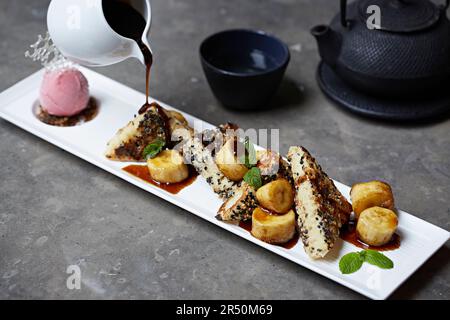 Pain japonais à la banane avec tranches de banane et glace à la fraise avec sauce au chocolat versée sur le dessus Banque D'Images