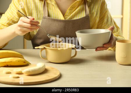 Une alimentation saine pour bébé. Femme mettant une délicieuse purée de banane dans un bol sur une table en bois clair, en gros plan Banque D'Images