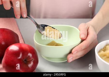 Une alimentation saine pour bébé. Femme mettant une délicieuse purée de pommes dans un bol à table gris clair, gros plan Banque D'Images