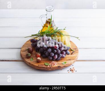 Raisins, poires, tomates, herbes et huile sur une planche de bois Banque D'Images