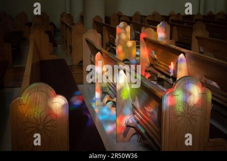 La lumière colorée des vitraux tombe sur les extrémités des bancs en bois sculptés à l'intérieur de la basilique cathédrale Saint-François d'Assise, Santa Fe, Nouveau-Mexique. Banque D'Images