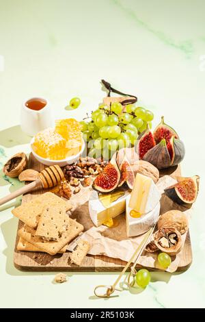 Camembert avec des craquelins, des fruits et du miel sur une planche à découper en bois Banque D'Images