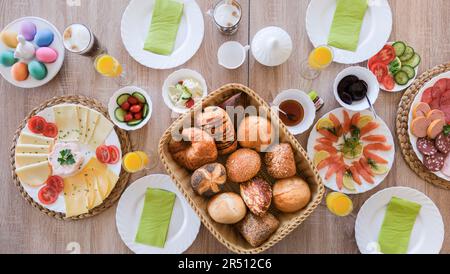 Une table de petit-déjeuner de Pâques est posée avec des œufs de couleur, des petits pains, du saumon et un plateau de fromages et de viandes Banque D'Images