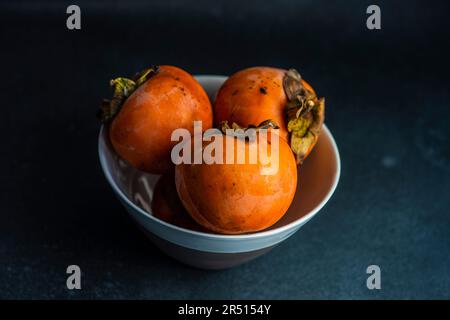 Des fruits mûrs persimmon dans le bol sur fond de pierre Banque D'Images