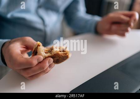 Photo rognée détaillée d'un homme d'affaires âgé méconnu aux mains ridées mangeant un hamburger avec du bœuf provenant d'un restaurant de restauration rapide Banque D'Images