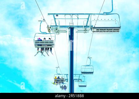 Groupe de skieurs qui remontent la montagne sur un télésiège en admirant la vue, vue d'en dessous, isolée contre le ciel bleu. Brochures de voyage et sport d'hiver Banque D'Images