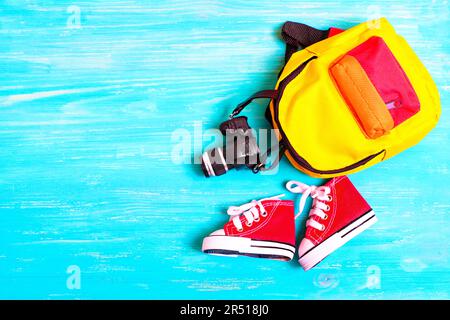 Chaussures en toile rouge pour tout-petits, sac à dos coloré et figurine miniature placée sur un fond en bois bleu. Concept lié à l'aventure créative. Banque D'Images