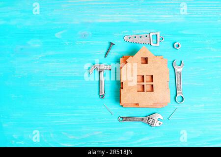 Modèle de maison en bois démontée accompagné de petites répliques en acier d'outils à main et de fixations, toutes placées sur un fond bleu. Bricolage, construction ou Banque D'Images