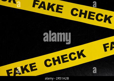 Concept de mise en garde et d'avertissement de faux chèques. Ruban de barricade jaune avec mot sur fond noir foncé. Banque D'Images