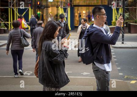 Un couple de touristes chinois s'arrête pour utiliser leur smartphone à Regent Street, Londres, Royaume-Uni. Banque D'Images