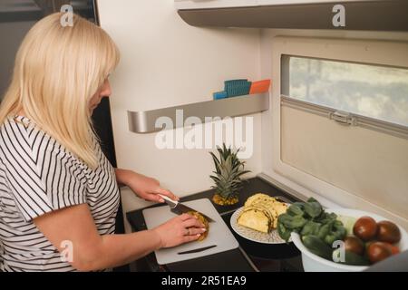 une femme cuisant de la nourriture dans la cuisine à l'intérieur d'un autocaravane, à l'intérieur d'un autocaravane. Banque D'Images