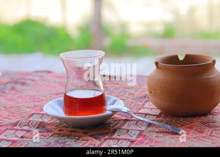 Photo prise en Turquie. La photo montre un petit verre de thé fort appelé - des armuts sur un tapis turc traditionnel étalé sur la table. Près d'un pot Banque D'Images