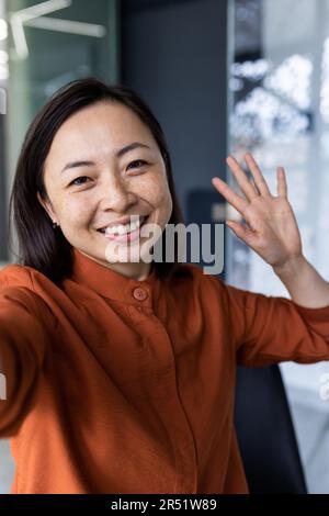 Prise de vue verticale, jeune femme d'affaires asiatique très belle qui parle lors d'un appel vidéo, agitant la caméra d'un smartphone à l'aide d'une application de communication à distance. Banque D'Images