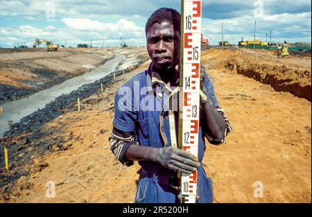 Mozambique, Maputo; Un homme arpentage des terres tandis que les ouvriers du bâtiment sont occupés avec un nouveau système de drainage pour la ville. Banque D'Images