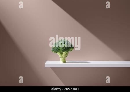 Bouquet de brocoli frais avec des feuilles vertes placées sur une table blanche sur fond marron en studio sous un rayon lumineux Banque D'Images