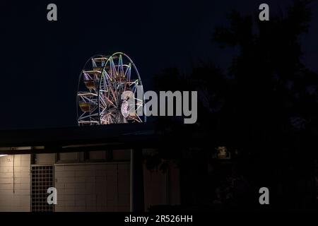 Vue lointaine d'une grande roue lumineuse contre le ciel nocturne. Banque D'Images