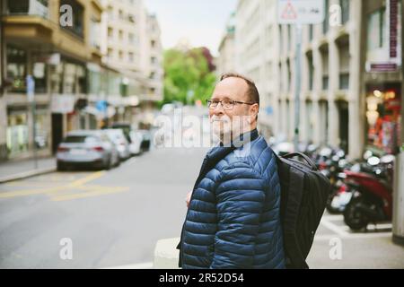 Portrait extérieur d'un homme de 55-60 ans portant une veste et un sac à dos bleus, en regardant vers l'arrière au-dessus de l'épaule Banque D'Images