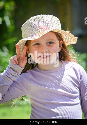 Jeune fille de 6 ans souriant et portant un chapeau de soleil lors d'une belle journée chaude au printemps au Royaume-Uni Banque D'Images