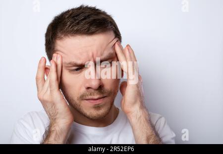 Portrait d'un jeune homme isolé sur fond gris souffrant de maux de tête graves, poussant les doigts vers les temples Banque D'Images