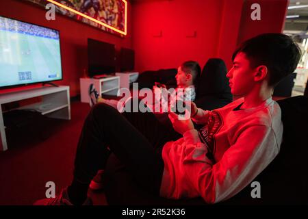 Deux gamers de garçons jouent à la console de jeu vidéo de manette de football dans la salle de jeu rouge. Banque D'Images