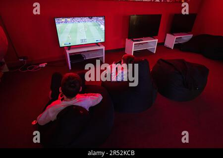 Deux gamers de garçons jouent à la console de jeu vidéo de manette de football dans la salle de jeu rouge. Banque D'Images