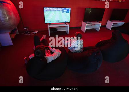 Deux gamers de garçons jouent à la console de jeu vidéo de manette de football dans la salle de jeu rouge. Banque D'Images