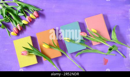 belles fleurs de printemps, rangée de fleurs de tulipes roses avec des livres sur fond violet, concept, plat, espace négatif, espace de copie libre Banque D'Images