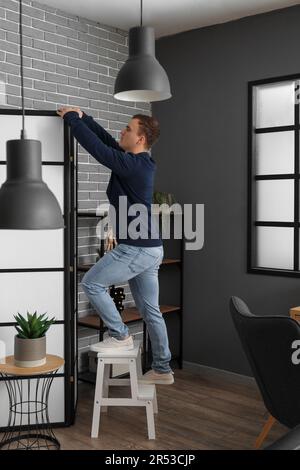 Jeune homme sur un escabeau près de l'écran rabattable dans la chambre Banque D'Images