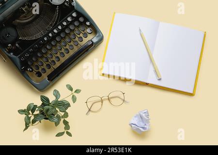 Machine à écrire vintage avec cahier ouvert, lunettes et plante sur fond jaune clair Banque D'Images