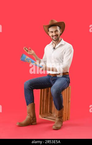 Beau cow-boy avec boussole et carte du monde assis sur fond rouge Banque D'Images