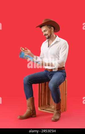 Beau cow-boy avec boussole et carte du monde assis sur fond rouge Banque D'Images