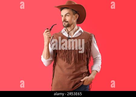 Beau cow-boy avec pipe de fumée sur fond rouge Banque D'Images