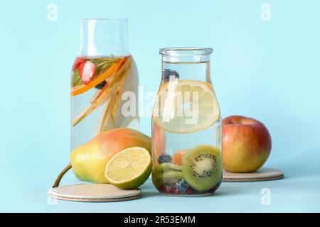 Bouteilles d'eau infusée avec différentes tranches de fruits sur fond bleu Banque D'Images