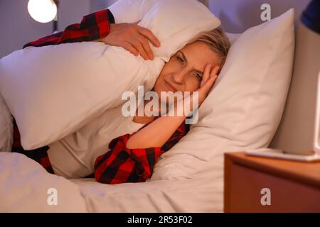 Femme mature avec oreillers couchés dans le lit la nuit Banque D'Images