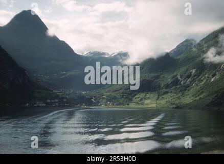 Geirangerfjord, Norvège. Vers. 1960 – Vue sur le village de Geiranger, Geirangerfjord et ses montagnes environnantes, prise d'un ferry. Banque D'Images