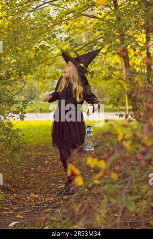 La petite sorcière regarde autour dans la peur et marche à travers la forêt avec une lanterne dans sa main. Banque D'Images