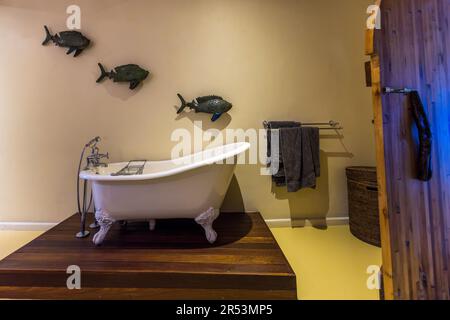 Salle de bains avec baignoire sur pied et décoration murale à Pumulani Lodge, Robin Pope Safaris, sur les rives du lac Malawi, Cape Maclear, dans le parc national du lac Malawi. Le poisson fabriqué à partir de matières premières recyclées est un élément de design du Pumulani Luxury Beach Lodge - Robin Pope Safaris Banque D'Images