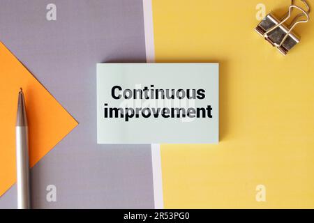 message texte d'amélioration continue sur le livre blanc et les fournitures de bureau, stylo, note papier, sur le bureau blanc, copier la vue de concept d'affaires d'espace de dessus, Banque D'Images