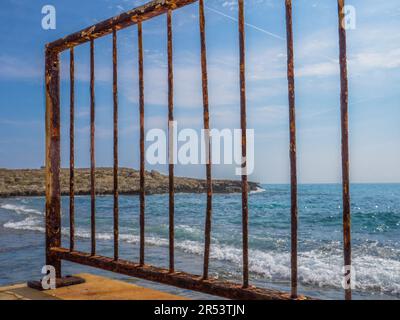 Vue depuis la jetée à travers la barrière de pont rouillé au-dessus de la mer Méditerranée et des rochers lors d'une journée ensoleillée à Aye Napa, Chypre. Banque D'Images