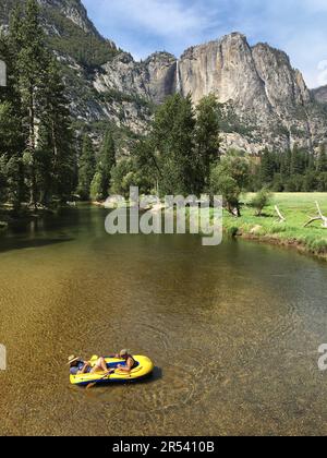 Un groupe de personnes apprécient une journée de vacances d'été relaxante flottant dans leur radeau sur la rivière Merced, en regardant une chute d'eau, dans le parc national de Yosemite Banque D'Images