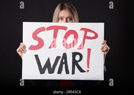 Femme tenant une affiche avec les mots Stop War sur fond noir Banque D'Images