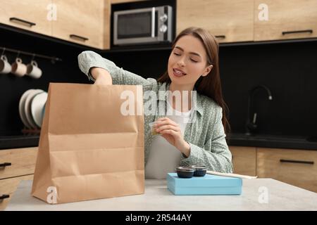 Belle jeune femme déballant sa commande du restaurant sushi à la table dans la cuisine Banque D'Images