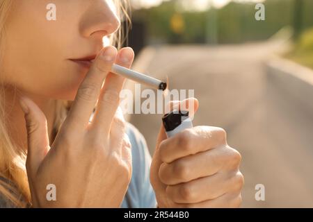 Jeune femme éclairant la cigarette à l'extérieur, gros plan des mains Banque D'Images