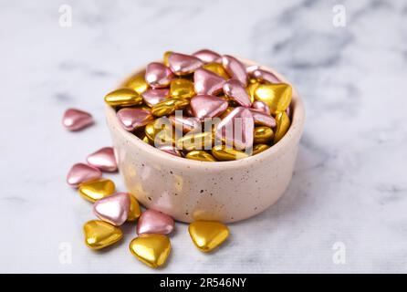 Bol et délicieux bonbons en forme de coeur sur une table en marbre blanc Banque D'Images